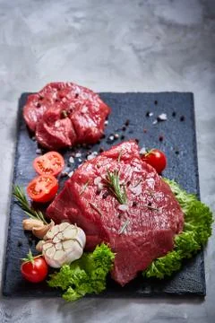 Composition of raw beefsteak on slate board with vegetables and seasoning Stock Photos