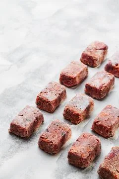 Composition with raw square cutlets on a light background. Natural dog food Stock Photos