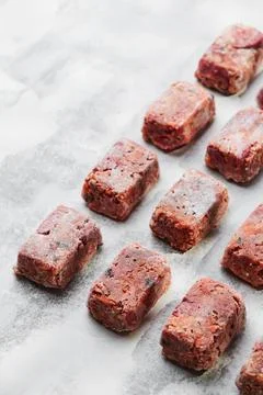 Composition with raw square cutlets on a light background. Natural dog food Stock Photos