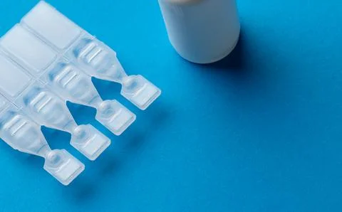 Composition of saline solution caplets and dropper bottle on blue background Stock Photos
