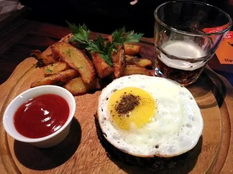 Composition of steak covered with fried egg, fried potatoes with sauce and be Stock Photos