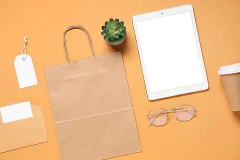 Composition with tablet computer, eyeglasses and delivery paper bag on orange Stock Photos