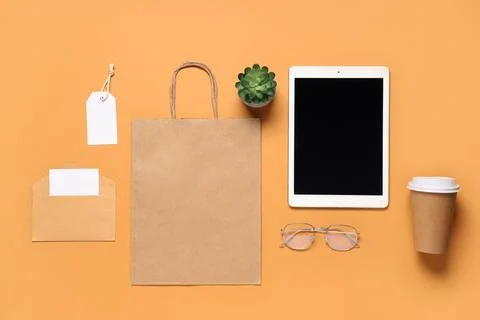 Composition with tablet computer, eyeglasses and delivery paper bag on orange Stock Photos
