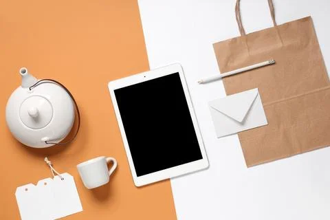 Composition with tablet computer, teapot and delivery paper bag on color back Stock Photos