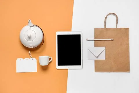 Composition with tablet computer, teapot and delivery paper bag on color back Stock Photos