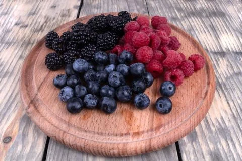 Composition of three types of summer berries laying on textured wooden plate Stock Photos
