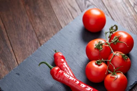 Composition of tomato bunch and hot pepper on black piece of board, top view Stock Photos