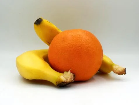 Composition of two bananas surrounding a single orange, creating a contrast Stock Photos