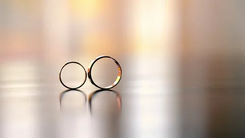 A composition of two gold wedding rings rolling on the table towards each other Stock Footage 253193300