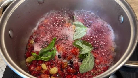 A compote of fresh berries, decorated with mint leaves, is brewed in a saucepan. Stock Footage 303973300