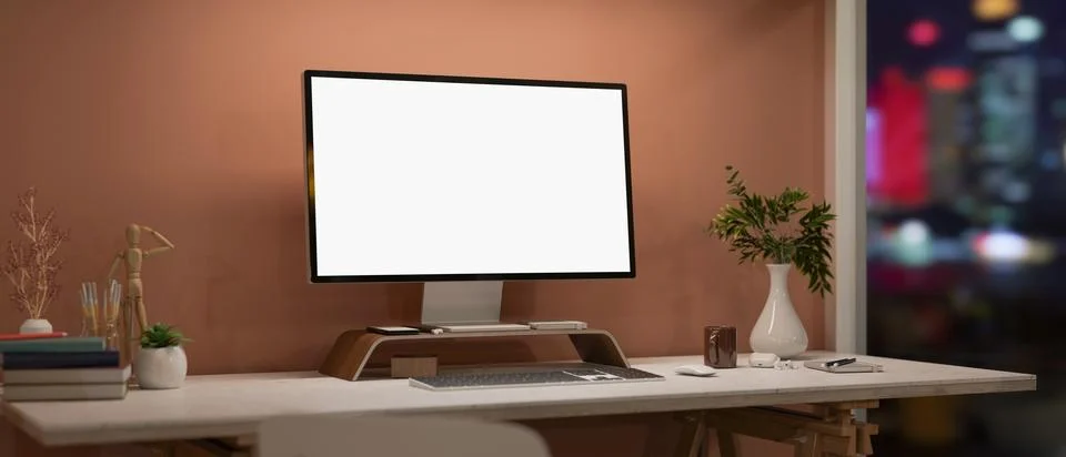A computer and decorative items on a white desk by the window at nighttime. Illustrazione stock