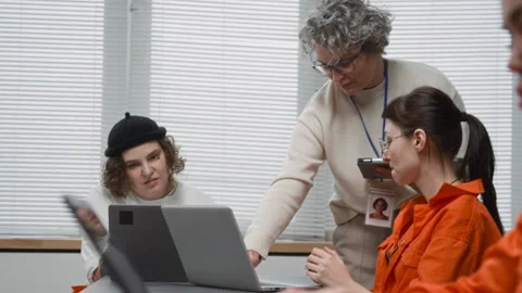 Computer Class in Prison with Mature Woman Assisting Inmates Using Laptops Stock Footage 329002040