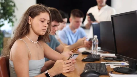 At computer class, young girl student sits with mobile phone and listens Stock Footage 268779369