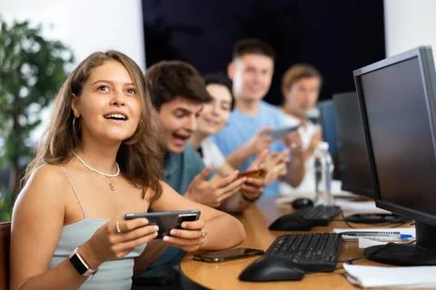 At computer class, young girl student sits with mobile phone and listens 库存照片