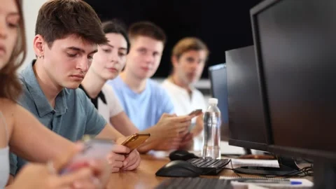 At computer class, young guy student sits with mobile phone and listens Stock Footage 273277062