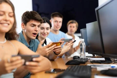At computer class, young guy student sits with mobile phone and listens Stockfoto's