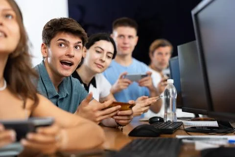 At computer class, young guy student sits with mobile phone and listens Stock Photos