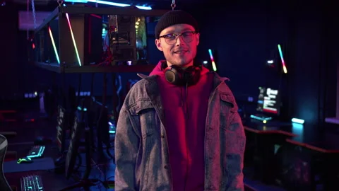 In a computer club in neon light, a young guy in a hat, glasses and a denim Stock Footage 152344818