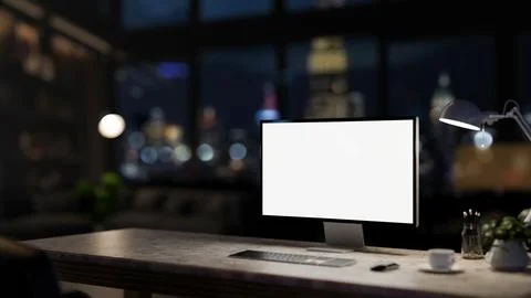 A computer desk in a modern dark office at night with a city view through t.. Stock Photos