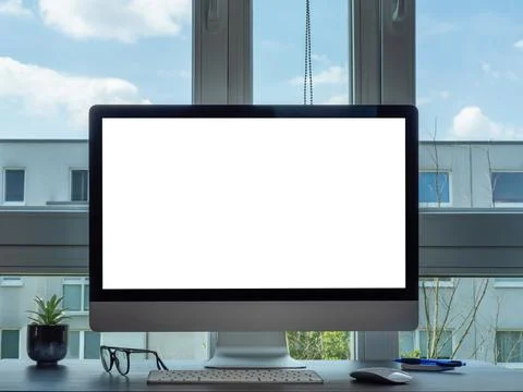 The computer is on the desk by the window. The computer has a white screen. Stock Photos