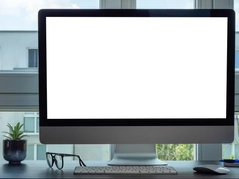 The computer is on the desk by the window. The computer has a white screen. Stock Photos