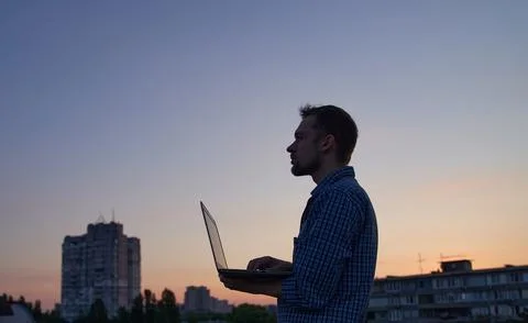 Computer developer in silhouette using laptop outdoor at sunset Stock Photos