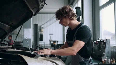 Computer diagnostics of cars, young mechanic specialist male uses laptop Stock Footage 303476747