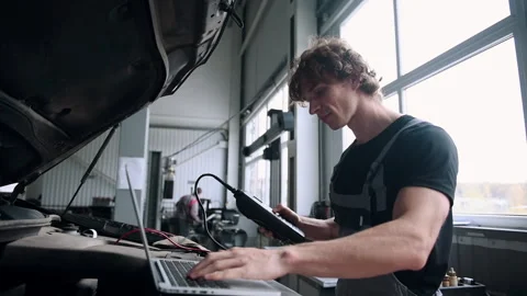 Computer diagnostics of cars, young mechanic specialist male uses laptop Stock Footage 303476837