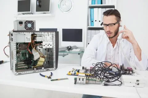 Computer engineer looking at broken device and making a phone call Stock Photos