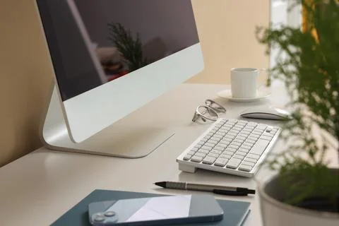 Computer with eyeglasses and cup of coffee on desk in office, closeup Stock Photos