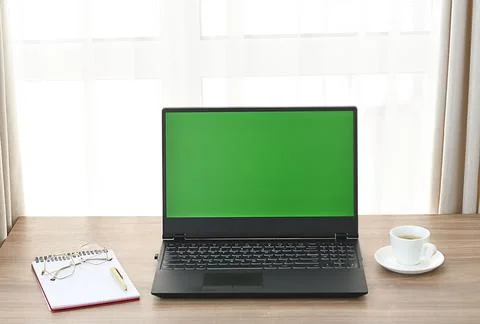 A computer with a green blank screen on a table with a notepad, glasses and a Stock Photos