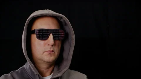 Computer hacker in hoodie and black sunglasses reflecting binary code on black Stock Footage 143906130