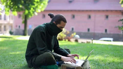 Computer hacker using laptop outside in sunny green park on urban background 스톡 동영상 139750714