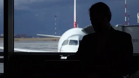 Computer hacker work on laptop at airport, incognito man sit against airliner Stock Footage 77062575