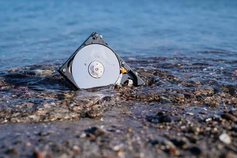 Computer hard disk lies in the shore sand of the sea and is washed by the wat Foto stock
