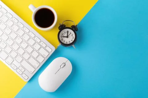 Computer keyboard and mouse with clock and coffee cup on yellow blue backgrou Stock Photos