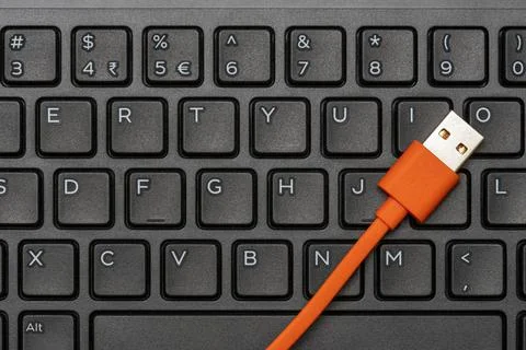 Computer keyboard and orange USB cable for data transfer Computer keyboard... Stock Photos