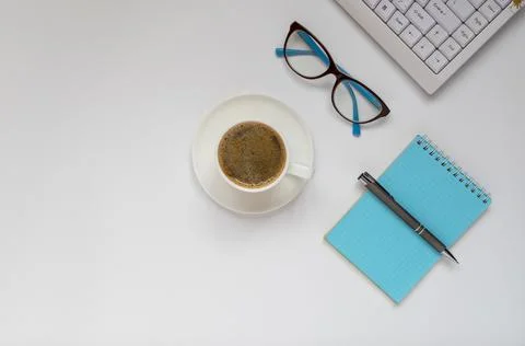 Computer keyboard, a cap of coffee, glasses, notepad and pen on a white surfa Stock Photos