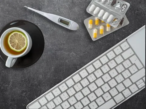 Computer keyboard, cup of tea, thermometer and blisters of pills. Stock Photos