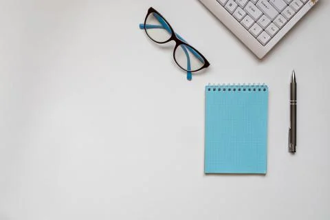 Computer keyboard, glasses, notebook and pen on a white surface. Stock Photos