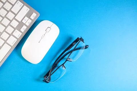 Computer keyboard, mouse and eyeglasses on blue background with copy space Stock Photos