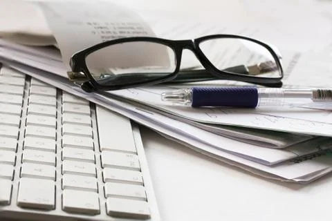 Computer keyboard, pair of glasses, pencil and messy papers lying on table Stock Photos