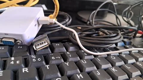 Computer keyboard with tangled cables. Messy workstation with electronic Stock Photos