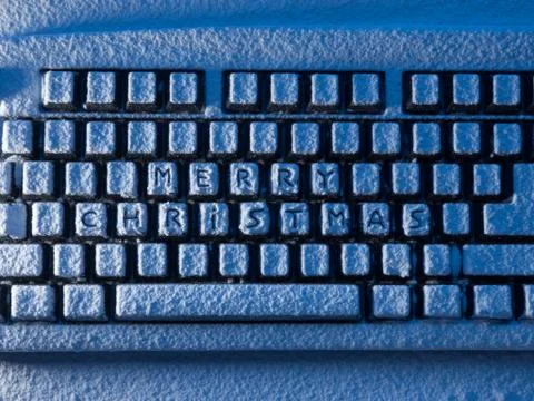 Computer keyboard with text merry christmas on buttons covered with snow lit by 스톡 사진
