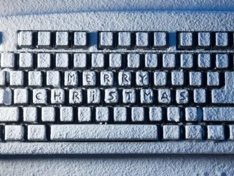 Computer keyboard with text merry christmas on buttons covered with snow lit by Foto stock