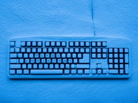 Computer keypad covered with snow illuminated by blue neon light with text merry Foto stock