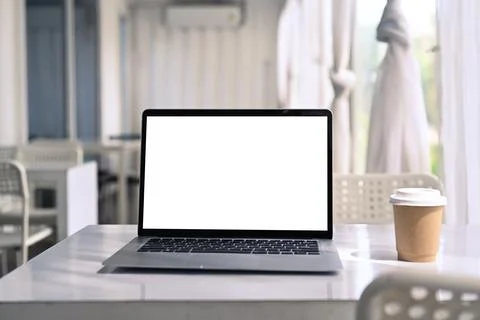 Computer laptop and coffee cup on white table in modern cafe. Stock Photos