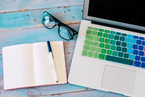 Computer laptop and paper notes with glasses on a blue wooden desktop viewed  Stock Photos