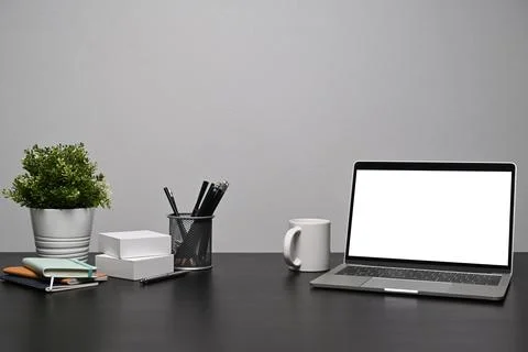 Computer laptop with blank display, coffee cup and supplies on black table. Stock Photos