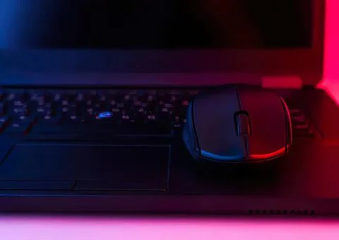 Computer laptop with mouse in dark pink and blue lighting Stock Photos